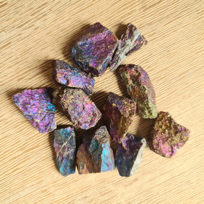 A collection of multicolored tumbled crystals with a metallic sheen, arranged on a wooden surface.