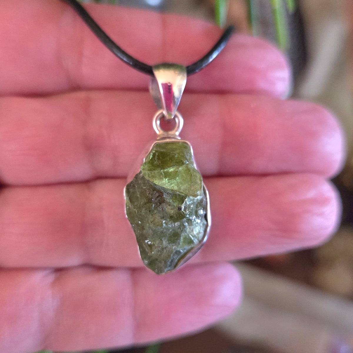 A hand holding a peridot pendant with a silver cap and a black cord.