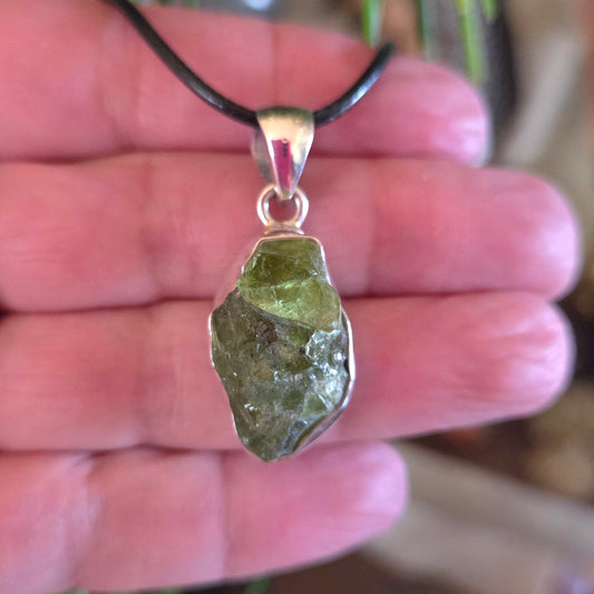 A hand holding a peridot pendant with a silver cap and a black cord.