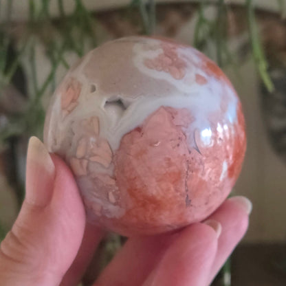 Hand holding a marbled stone with pink and white patterns against a blurred natural background