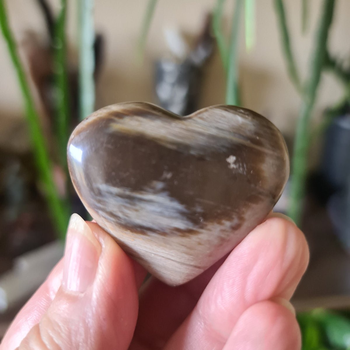 A hand holding a heart-shaped petrified wood charm with a brown and beige color pattern.