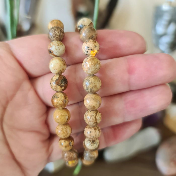 A hand holding a bracelet with Picture Jasper beads, with varying shades of brown and beige.