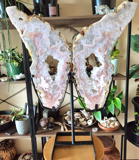 A pair of pink amethyst crystal figurines shaped like angel wings, displayed on a stand.