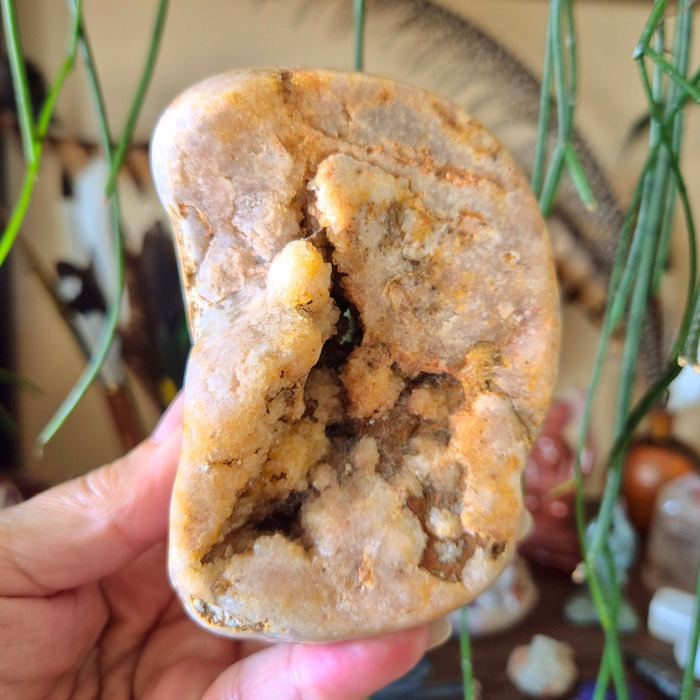 A polished pink amethyst freeform held in a person's hand, with a blurred background.