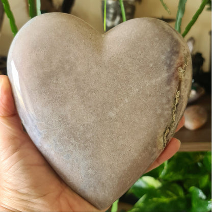A hand holding a polished pink amethyst heart-shaped crystal stone.