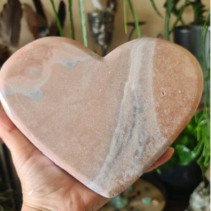 A hand holding a polished pink amethyst heart-shaped crystal.