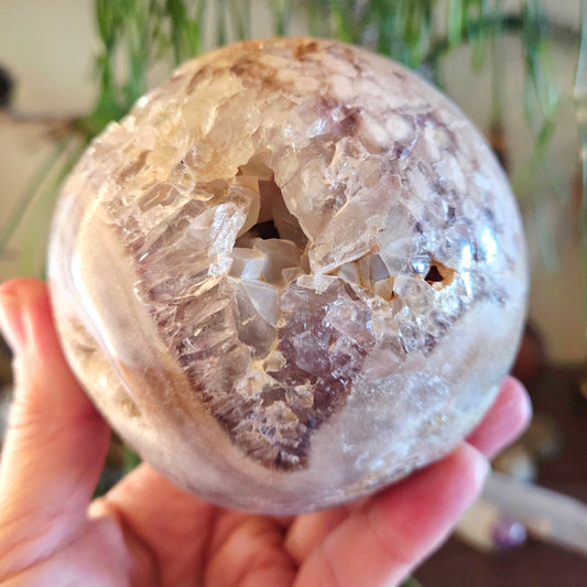 A hand holding a pink amethyst crystal sphere with a visible hollow center.