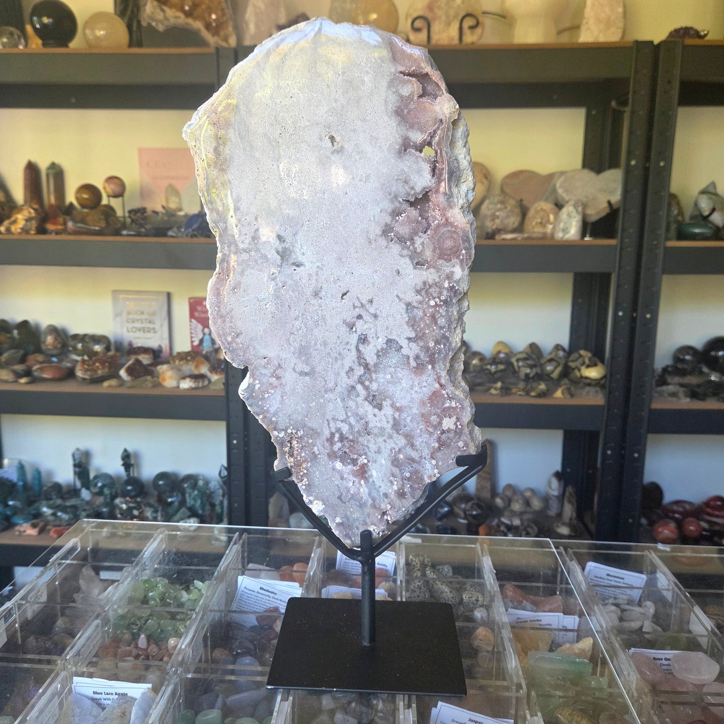 Large crystal on a stand in a store setting with shelves of various items in the background