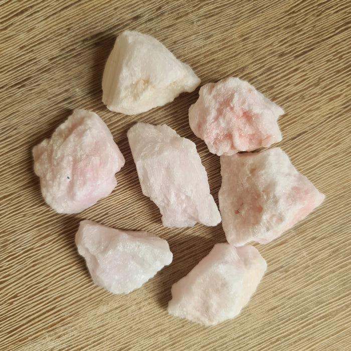 A collection of polished pink aragonite chunks on a wooden surface.