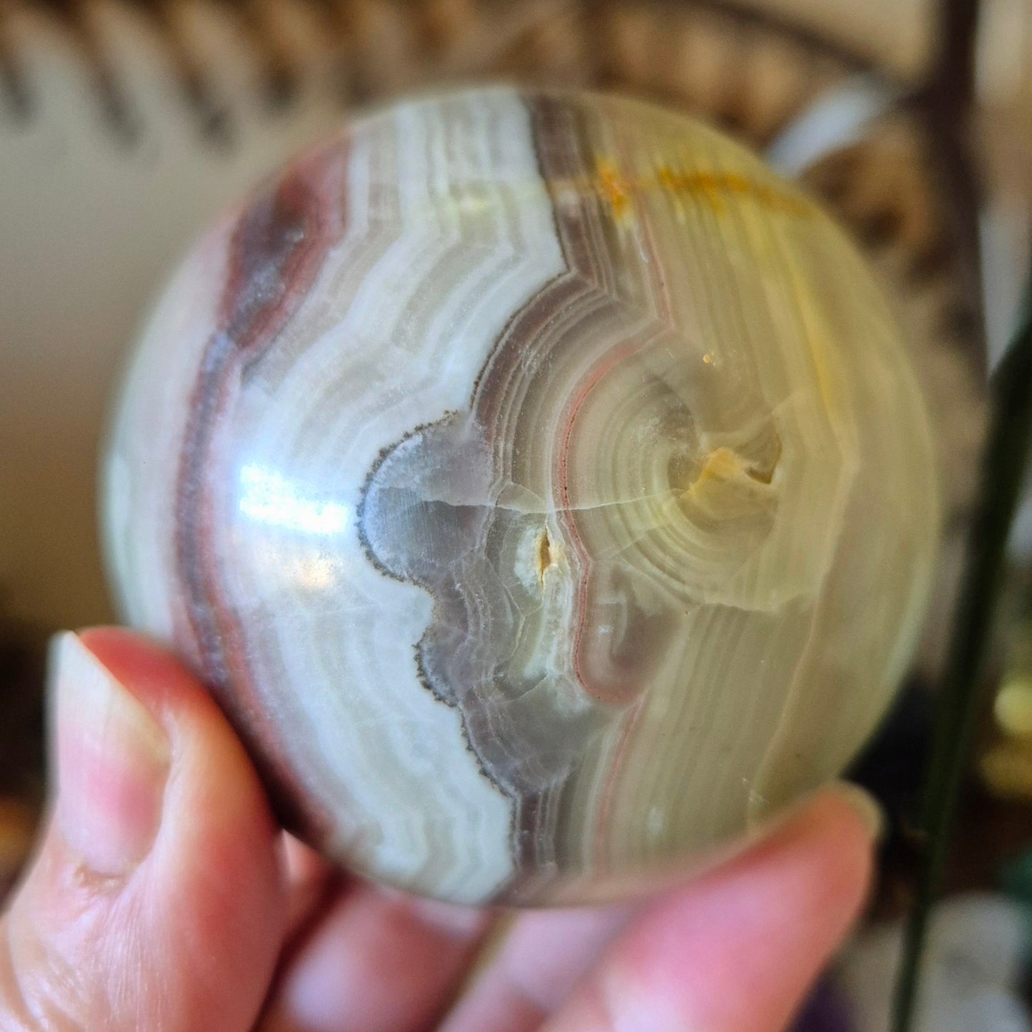 A close-up image of a polished pink onyx sphere held in a person's hand.