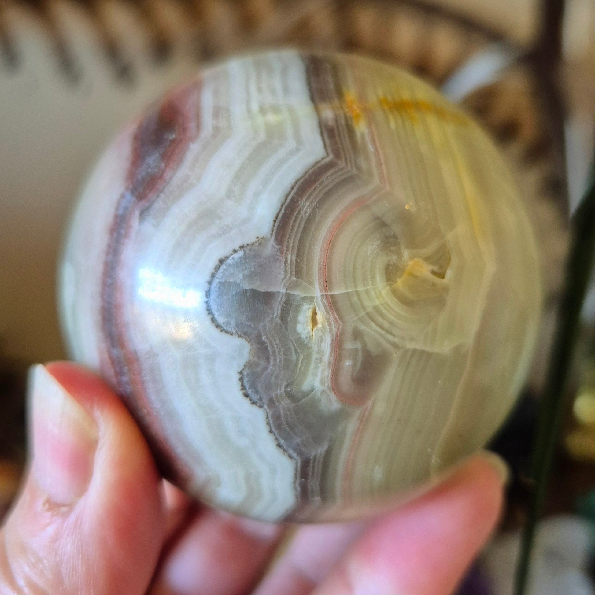 A close-up image of a polished pink onyx sphere held in a person's hand.