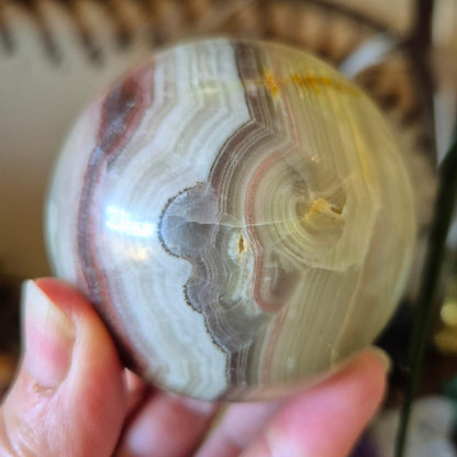 A close-up image of a polished pink onyx sphere held in a person's hand.