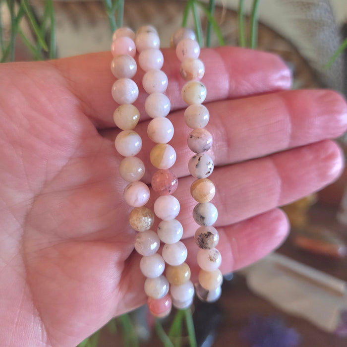 Hand holding two beaded bracelets with a blurred natural background