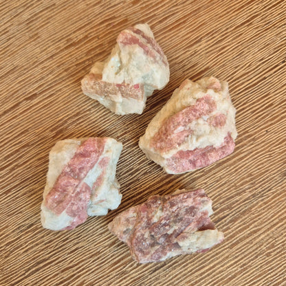 A collection of pink tourmaline chunks placed on a wooden surface.