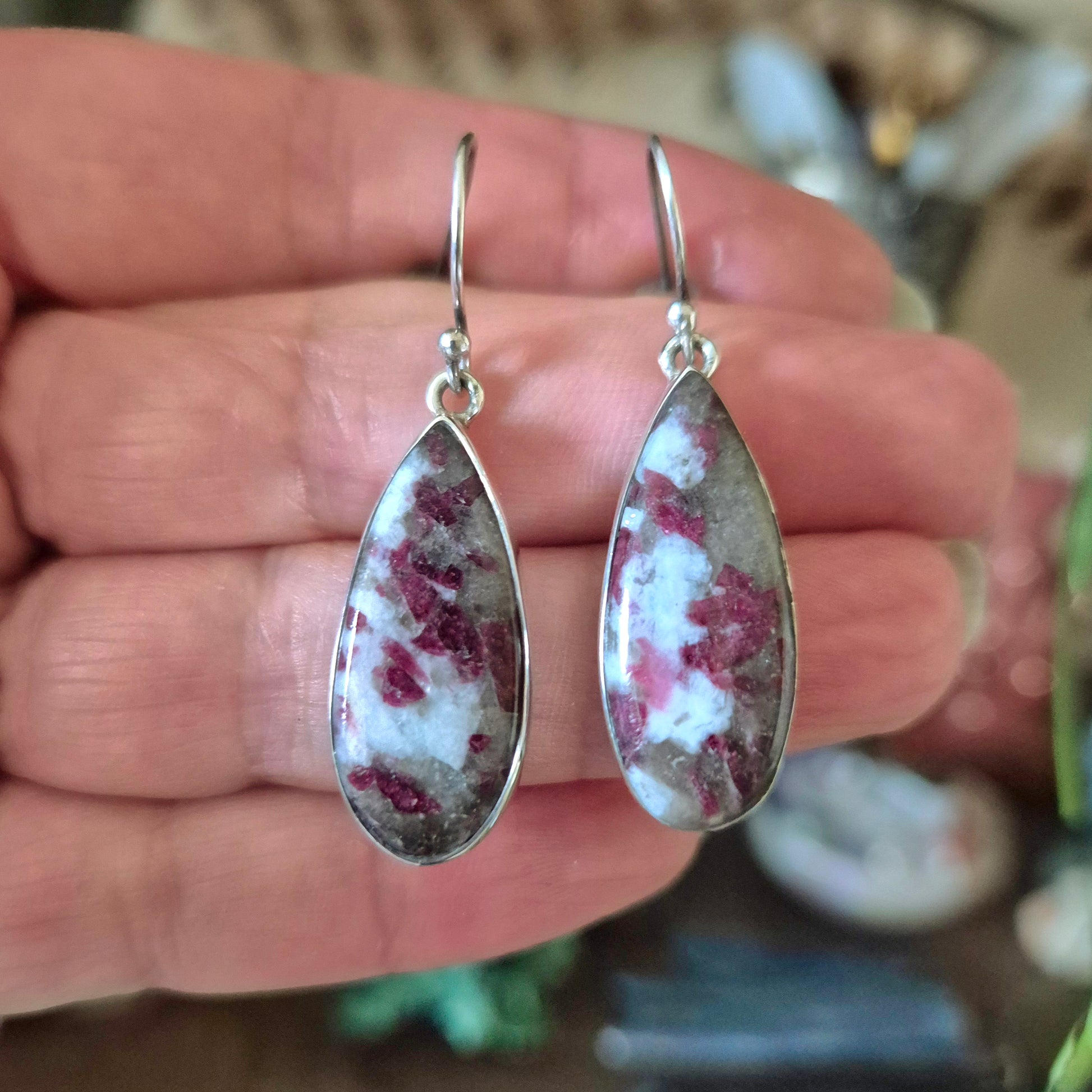 A pair of silver-colored pink tourmaline earrings held in a person's hand.