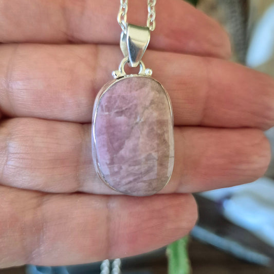 A hand holding a pink tourmaline faceted pendant with a silver mounting and chain.