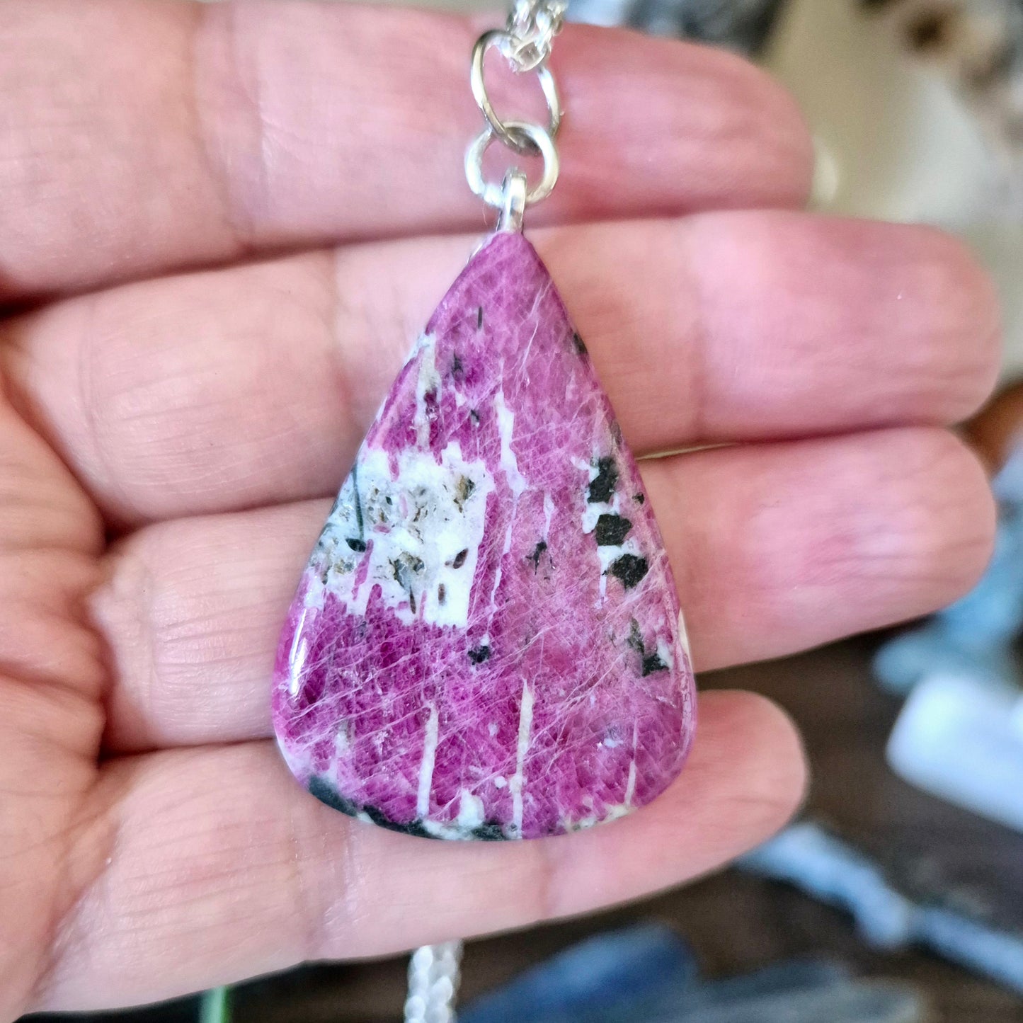 A teardrop-shaped pink tourmaline pendant with white and black inclusions, held in a person's hand.