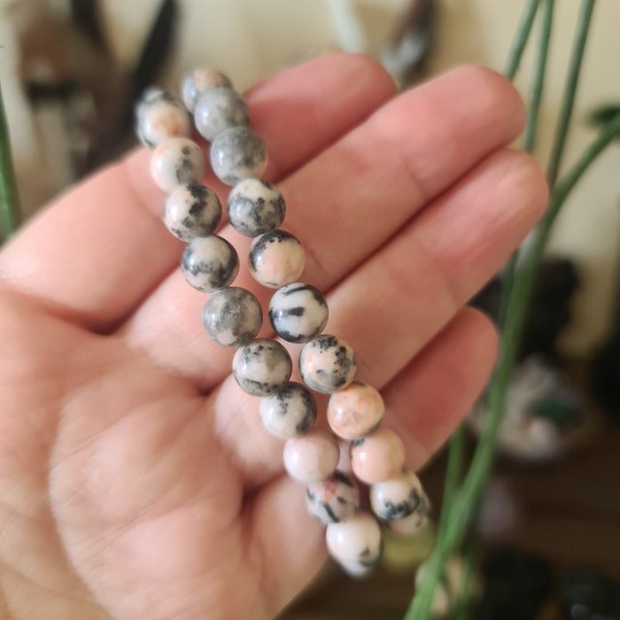 A hand holding a pink and black zebra jasper beaded bracelet.