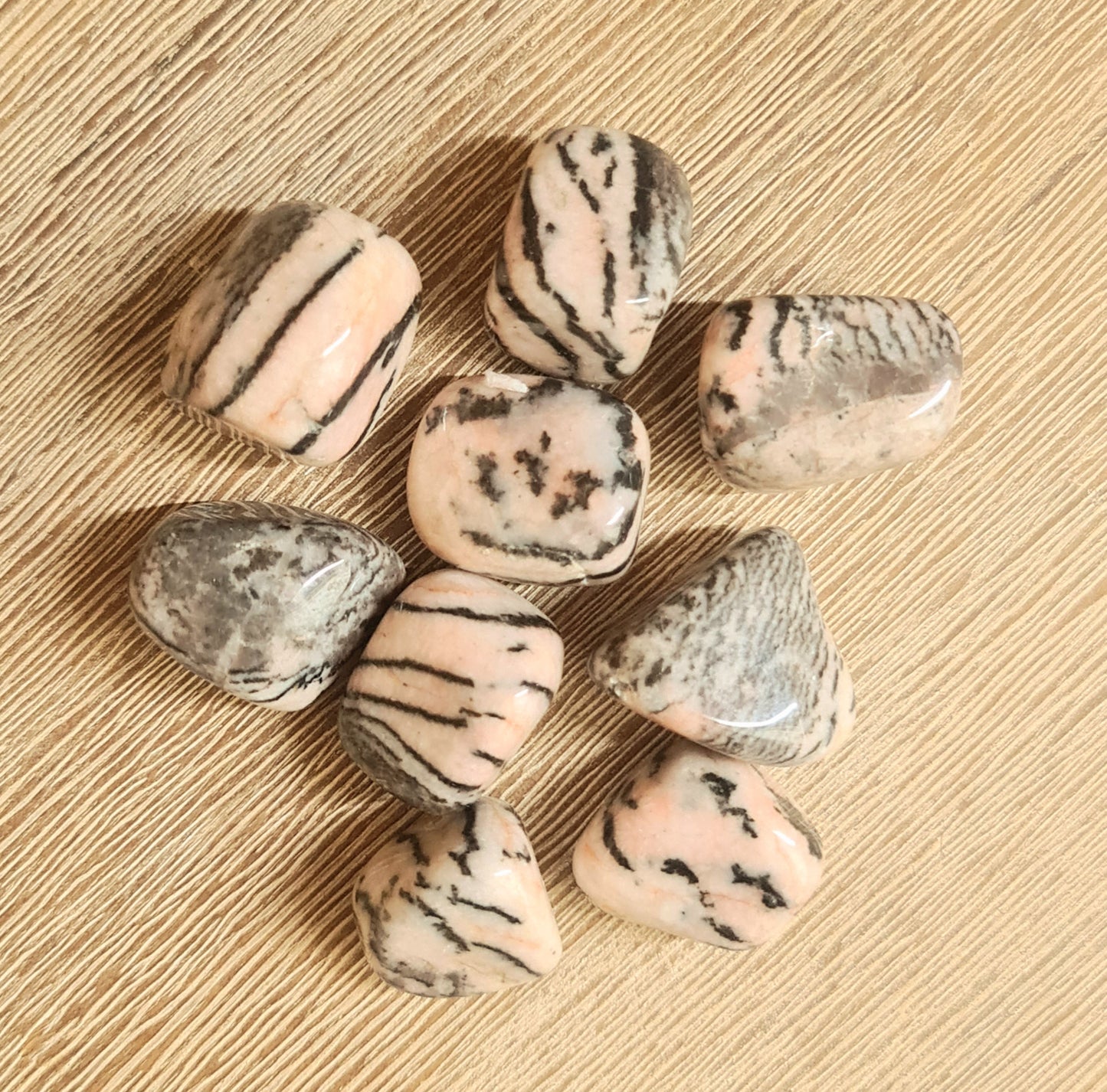 A collection of pink zebra jasper tumbles with black stripes on a wooden surface.