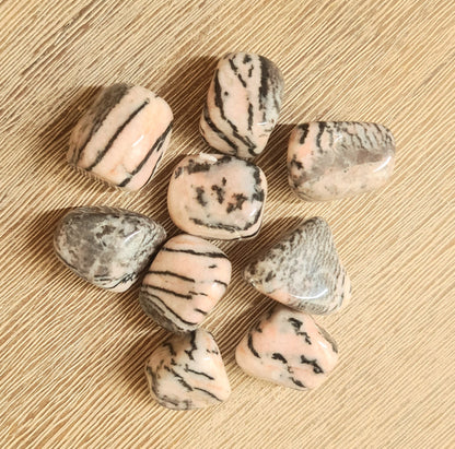 A collection of pink zebra jasper tumbles with black stripes on a wooden surface.