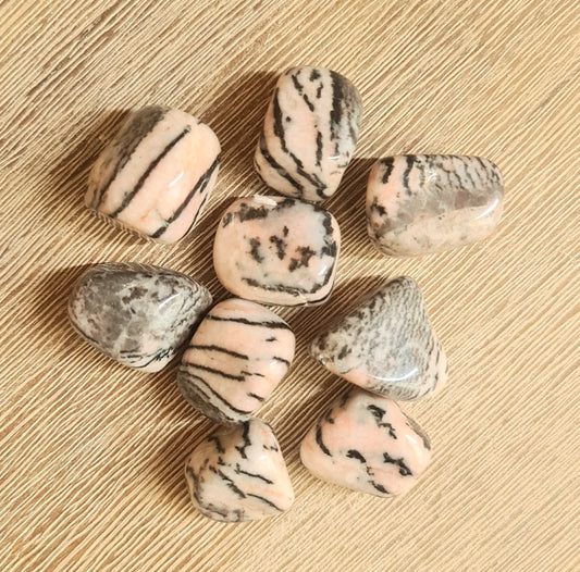 A collection of pink zebra jasper tumbles with black stripes on a wooden surface.