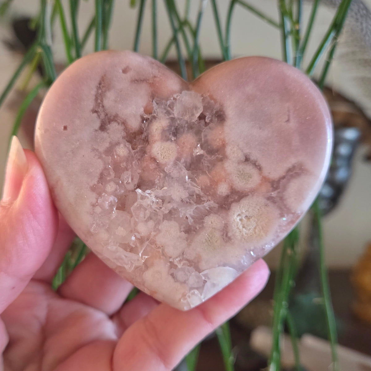 Heart-shaped crystal stone held in a hand with a blurred background