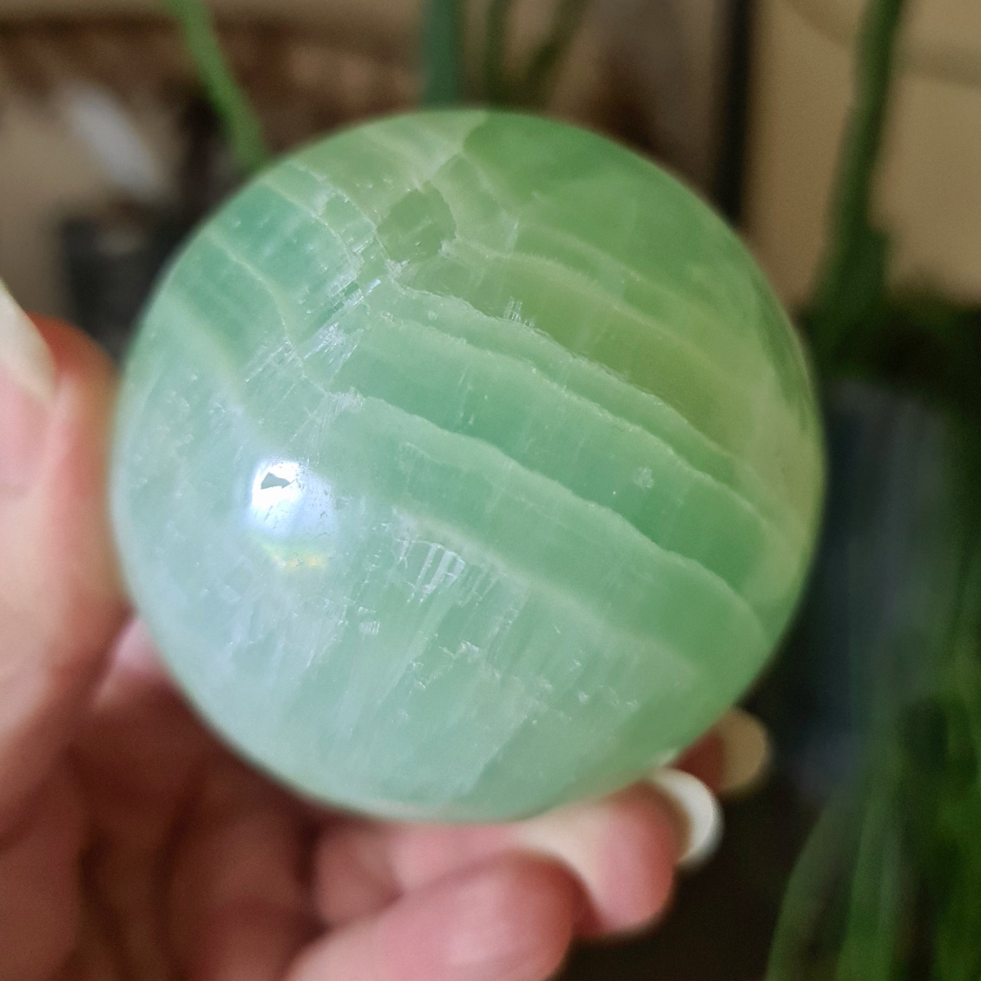 A polished green Pistachio Calcite sphere held in a person's hand.