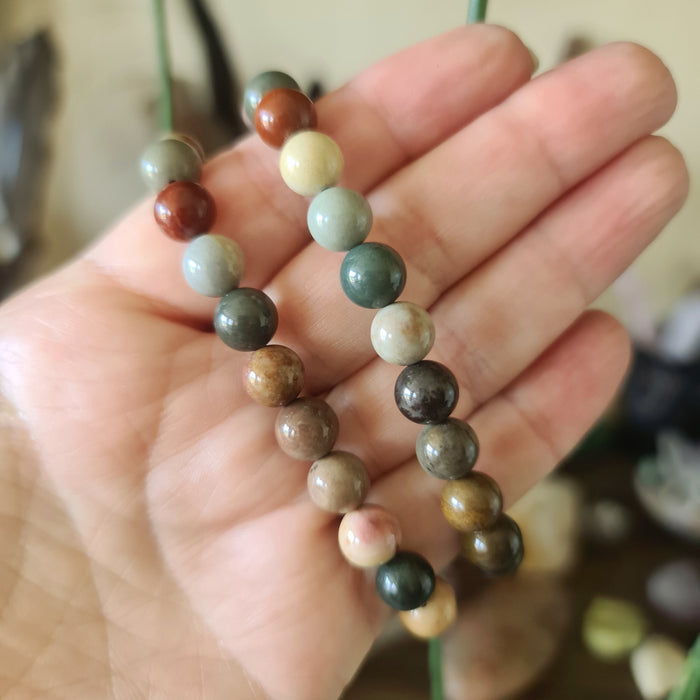 A multicolored beaded bracelet with a variety of geometric shaped beads, held in a person's hand.