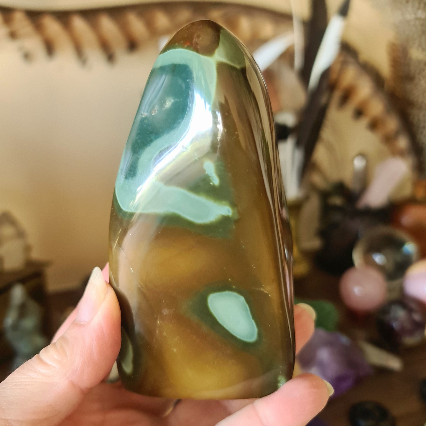 A polychrome jasper freeform stone held in a person's hand, with a green and brown color pattern.