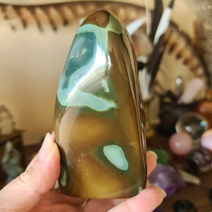 A polychrome jasper freeform stone held in a person's hand, with a green and brown color pattern.