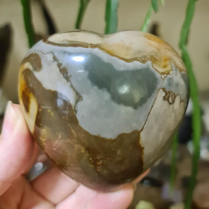 A polished heart-shaped stone with a marbled brown and beige color pattern, held in a person's hand.