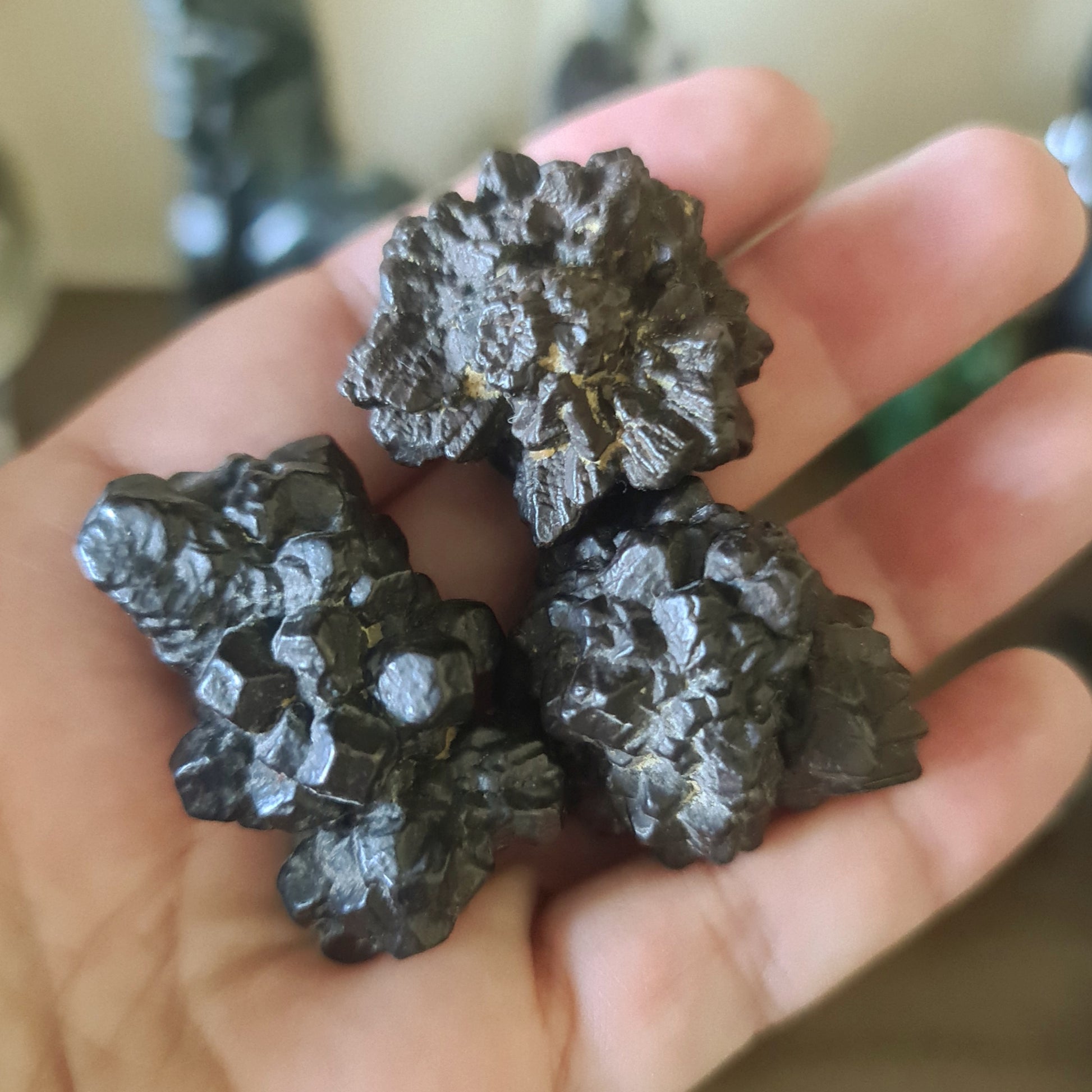 A hand holding three black tumbled crystals, with visible natural crystal patterns and color variations.