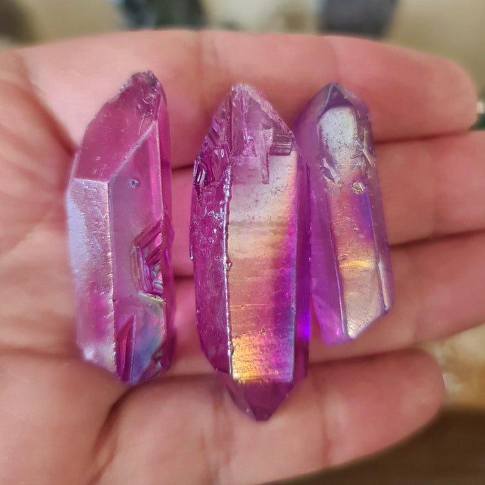 A hand holding a purple aura quartz crystal with iridescent colors and a metallic sheen.