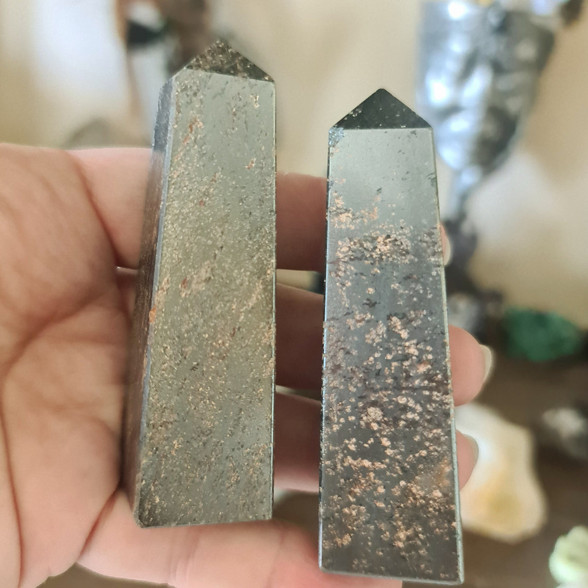 Two polished pieces of pyrite, one larger and one smaller, held in a person's hand, with a blurred background suggesting indoor setting.