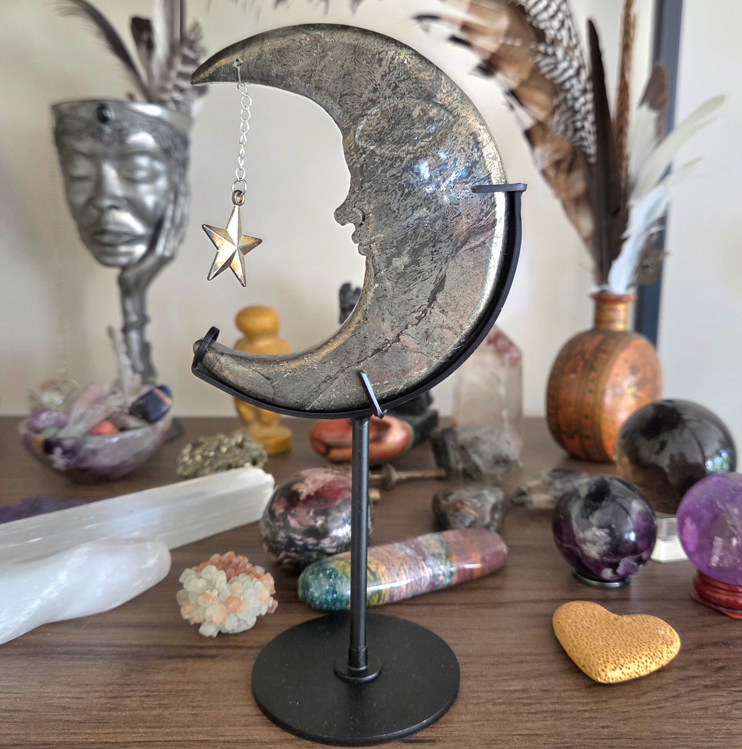 Decorative moon and star sculpture on a stand with crystals and other objects in the background