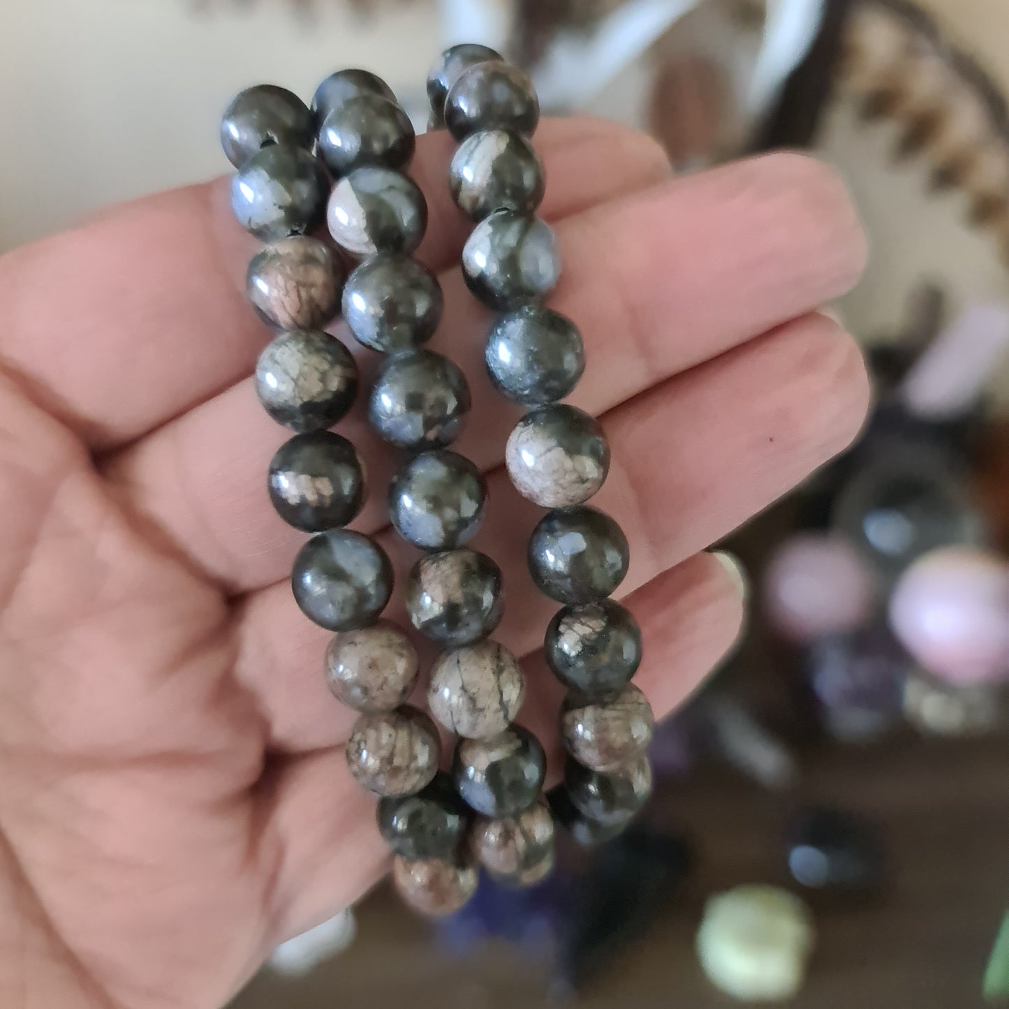 A hand holding a beaded bracelet with a mix of dark and light brown stones.