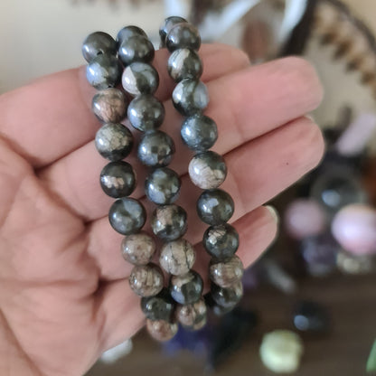 A hand holding a beaded bracelet with a mix of dark and light brown stones.