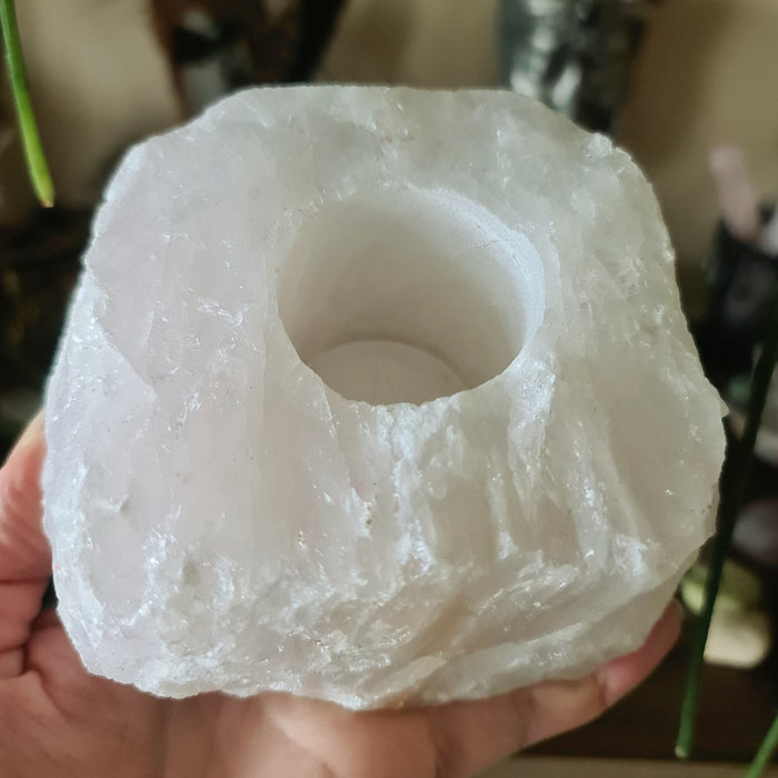 A person holding a Rose Quartz tealight holder with a lit candle inside, showcasing the pink crystal's interior.