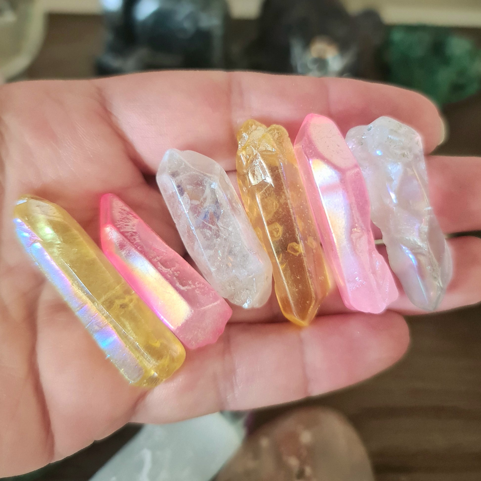 A collection of multicolored aura quartz crystals held in a person's hand, featuring a mix of pink, yellow, and clear colors.