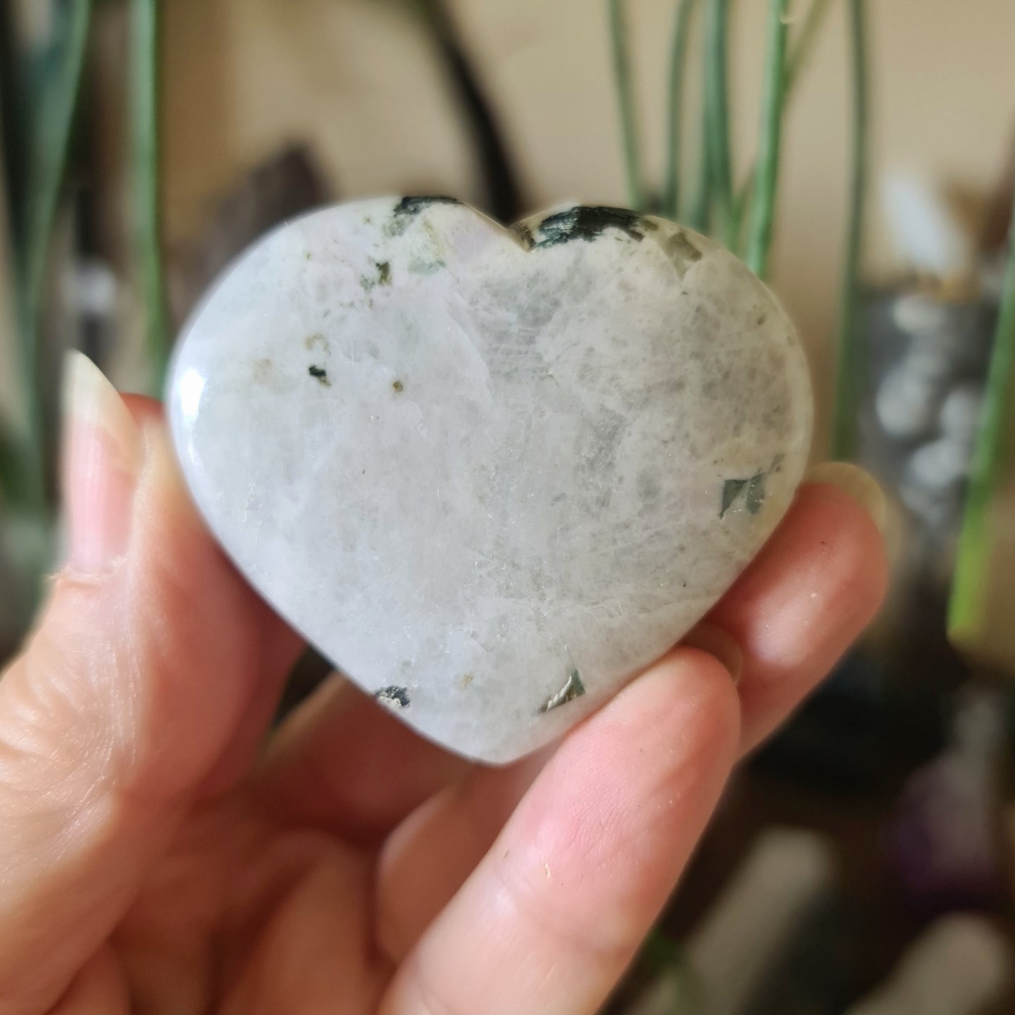 A hand holding a polished Rainbow Moonstone heart-shaped crystal.