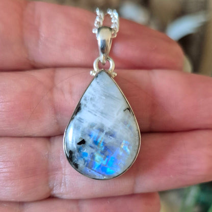 A silver-colored rainbow moonstone pendant held in a hand, with a chain loop for attachment.