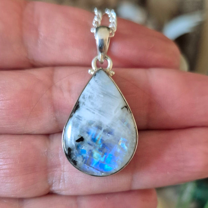 A silver-colored rainbow moonstone pendant held in a hand, with a chain loop for attachment.