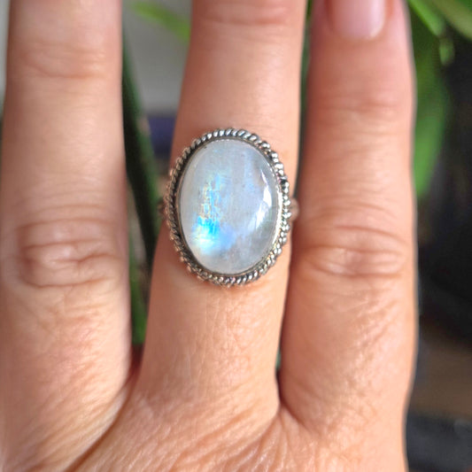 Silver ring with a gemstone on a person's finger against a blurred natural background