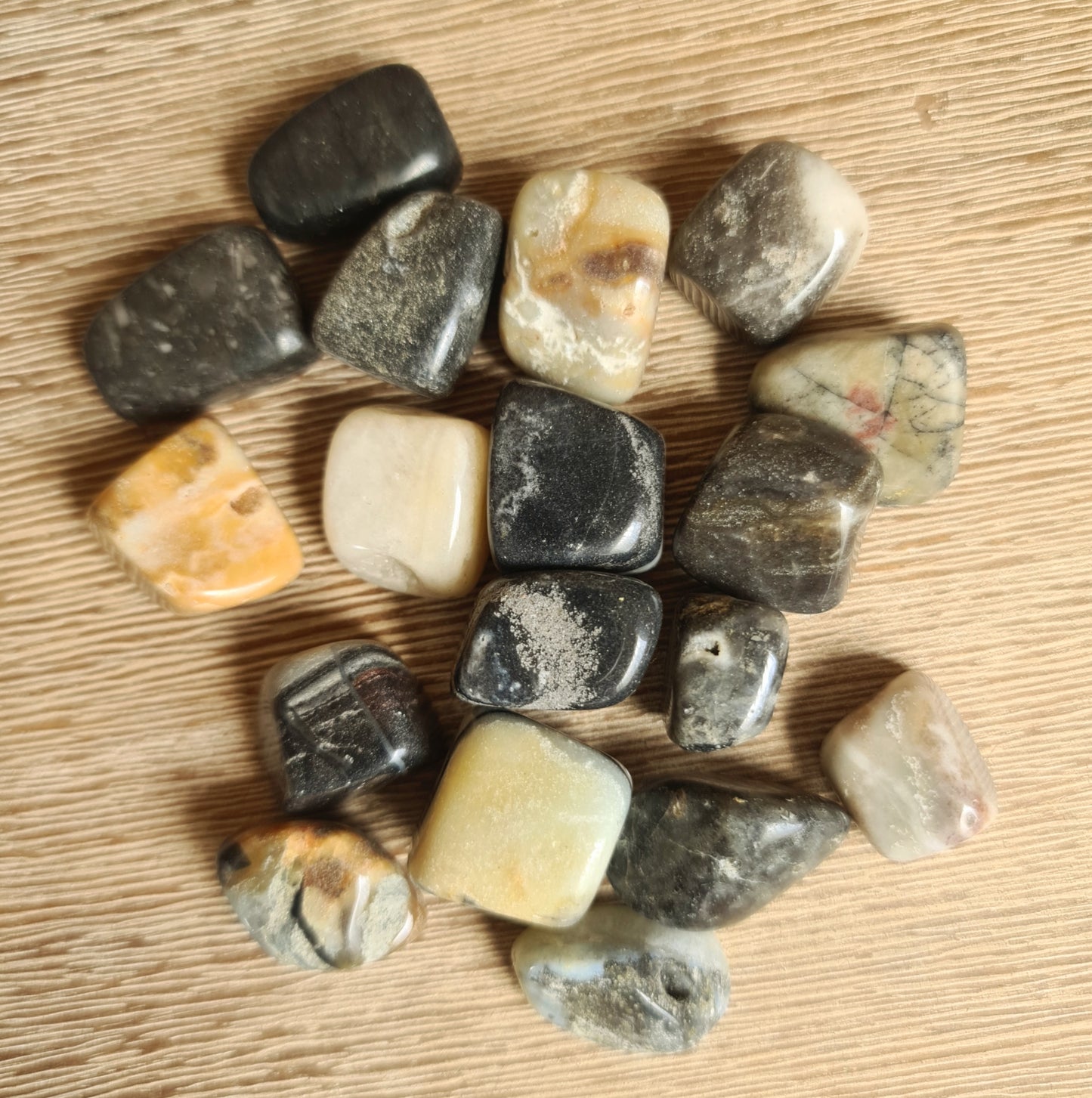 A collection of various colored polished jasper tumbles on a wooden surface.