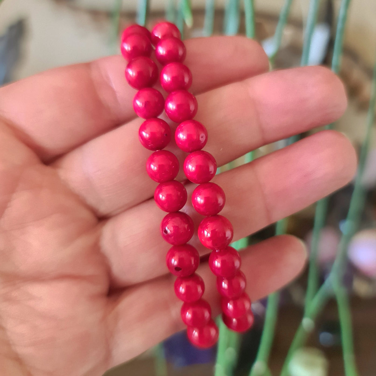 A person holding a red coral bracelet with round beads.