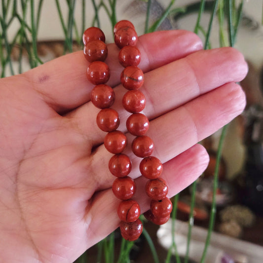A hand holding a red jasper bracelet with round beads.