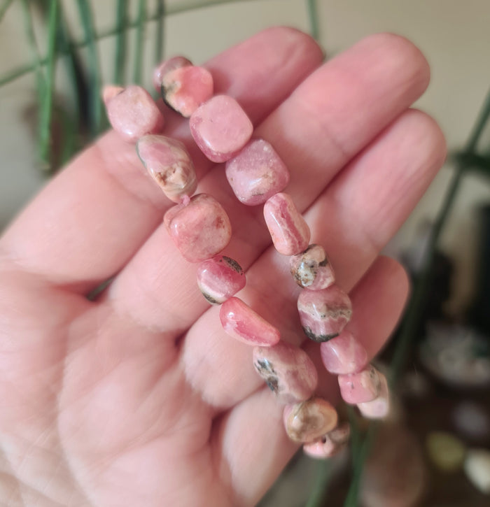 A hand holding a series of pink, irregularly shaped rhodochrosite pebble beads.