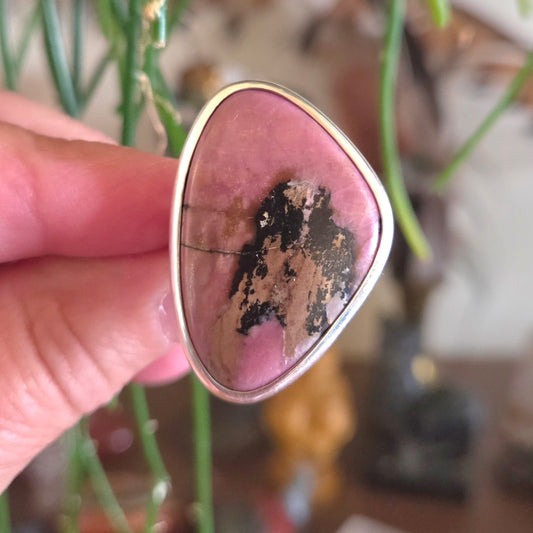 Pink stone with gold frame held by a hand against a blurred natural background
