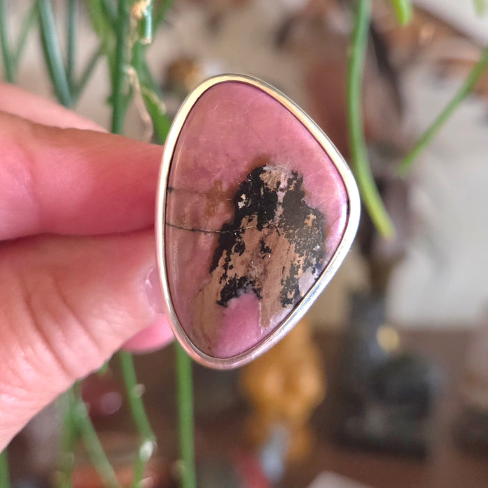 Pink stone with gold frame held by a hand against a blurred natural background