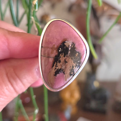 Pink stone with gold frame held by a hand against a blurred natural background